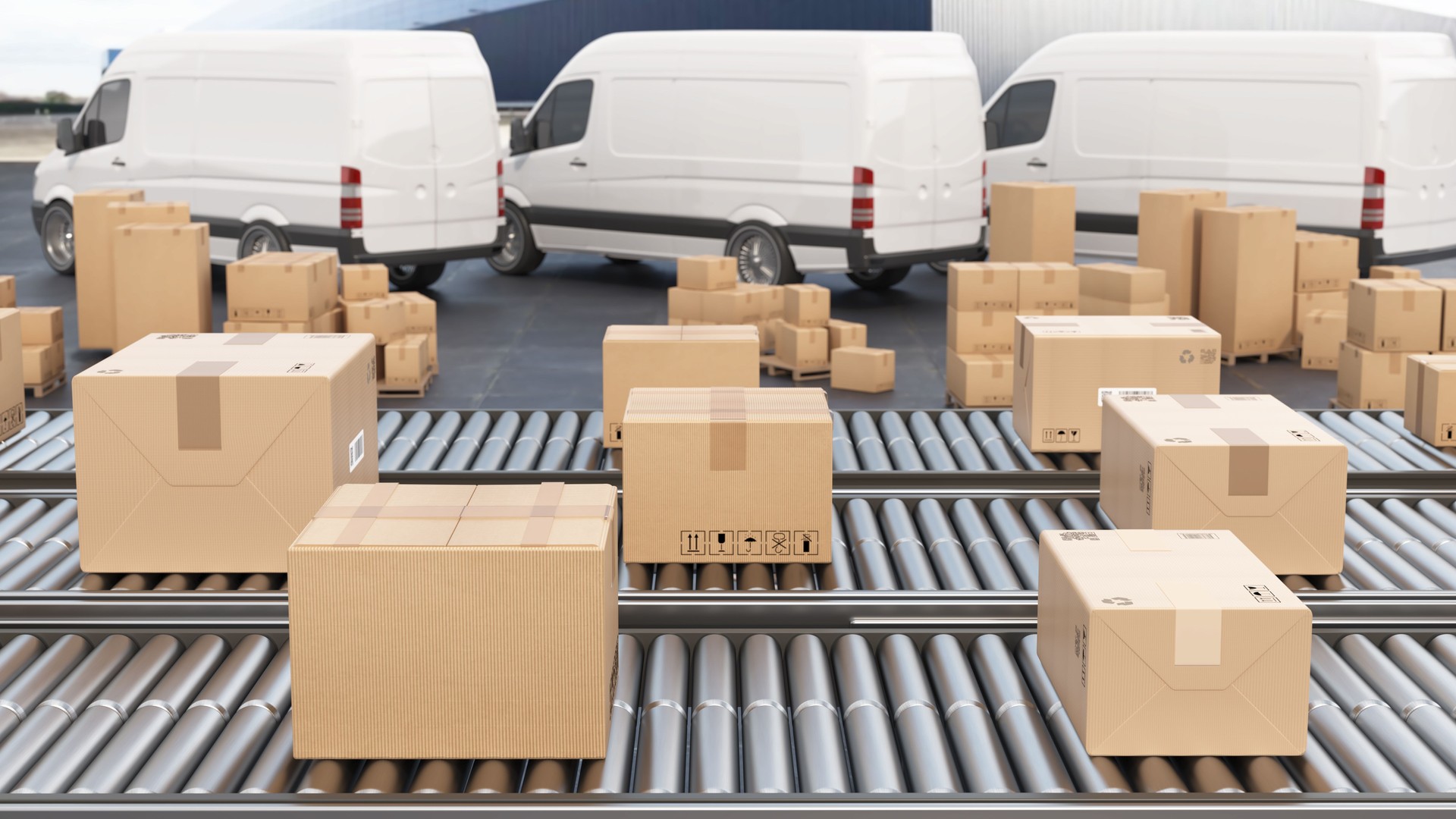 Packages moving through a conveyor system at a distribution center with delivery vans in the background during daylight hours